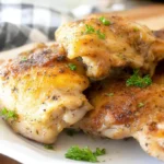 Golden-brown Baked Boneless Skinless Chicken Thighs Recipe served on a white plate with fresh parsley.