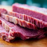 Close-up of perfectly cooked, sliced corned beef on a wooden board, showcasing the delicious outcome when learning how to make corned beef from scratch.