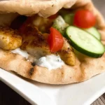 Close-up of a delicious Mediterranean Chicken Gyros Recipe on a white plate, filled with chicken, tzatziki, cucumber, and tomato.