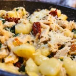 Appetizing Dump and Go Marry Me Chicken gnocchi dish with creamy sauce, shredded chicken, spinach, and cheese in a dark pan.