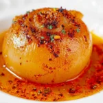 Close-up of a perfectly cooked onion boil, garnished with vibrant spices, served in a white bowl.