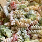 Close-up of a vibrant Ranch Pasta Salad with tri-color rotini, broccoli, tomatoes, and cucumbers in a creamy dressing.