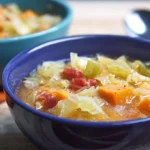 Two warm bowls of homemade Weight Loss Cabbage Soup with vegetables and a spoon on a wooden table.